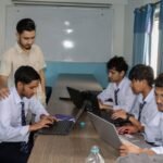 IT students participating in a bootcamp at Texas International College—a man instructor in a white shirt teaching four boys, students, to work on a laptop